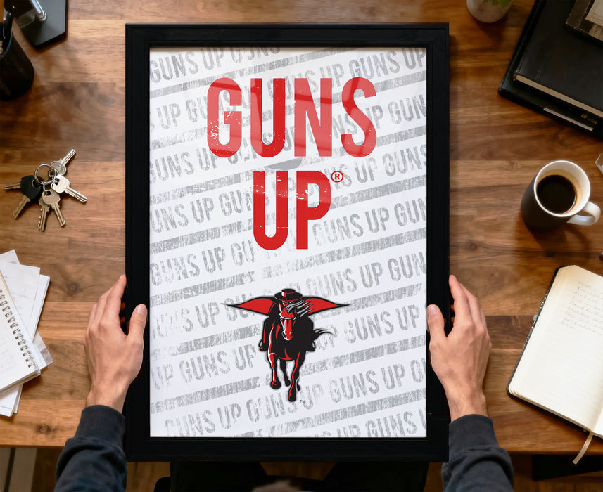 A person is holding up a framed poster with the text "GUNS UP" on it, which appears to be a promotional or advertising material.