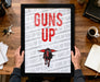 A person is holding up a framed poster with the text "GUNS UP" on it, which appears to be a promotional or advertising material.