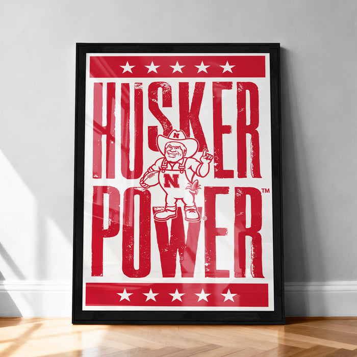 A framed poster with the text "HUSKER POWER" and an illustration of a character wearing a cowboy hat and holding a sign.