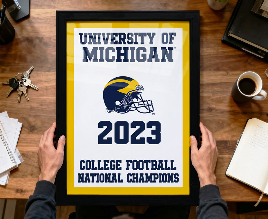 A framed poster titled "UNIVERSITY OF MICHIGAN" with a football helmet and the year "2023" displayed, along with the text "COLLEGE FOOTBALL NATIONAL CHAMPIONS".