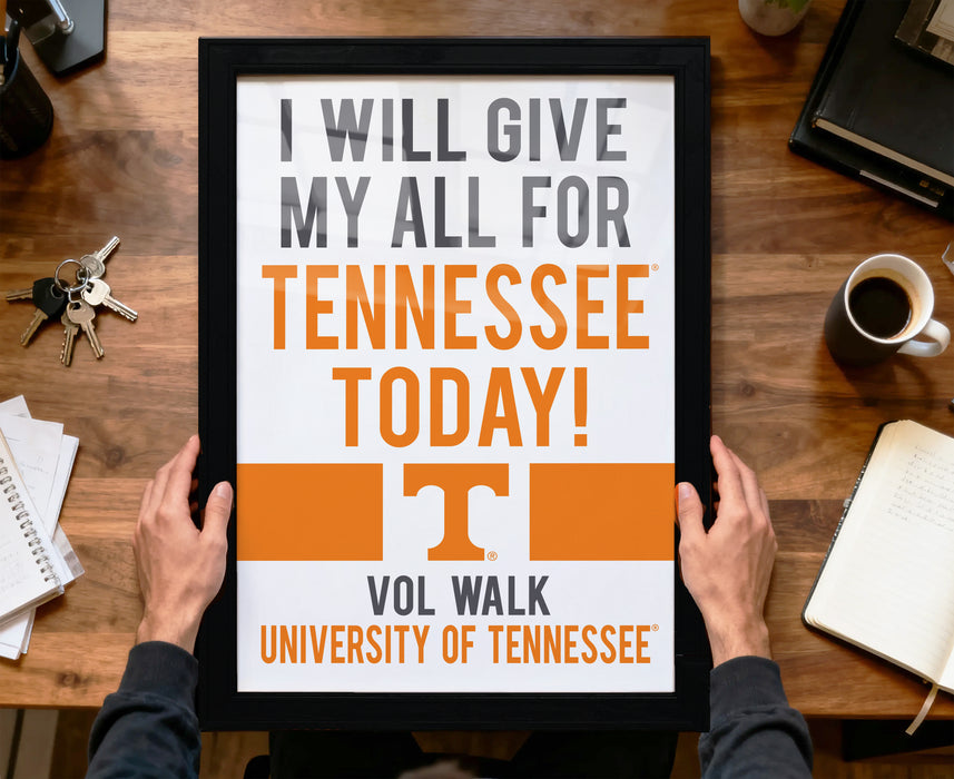 A person is holding up a framed sign with the text "I WILL GIVE MY ALL FOR TENNESSEE TODAY!" The sign is for the "VOL WALK UNIVERSITY OF TENNESSEE".