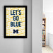 a framed poster with the text "LET'S GO BLUE" on it, which is displayed on a wall in a room.