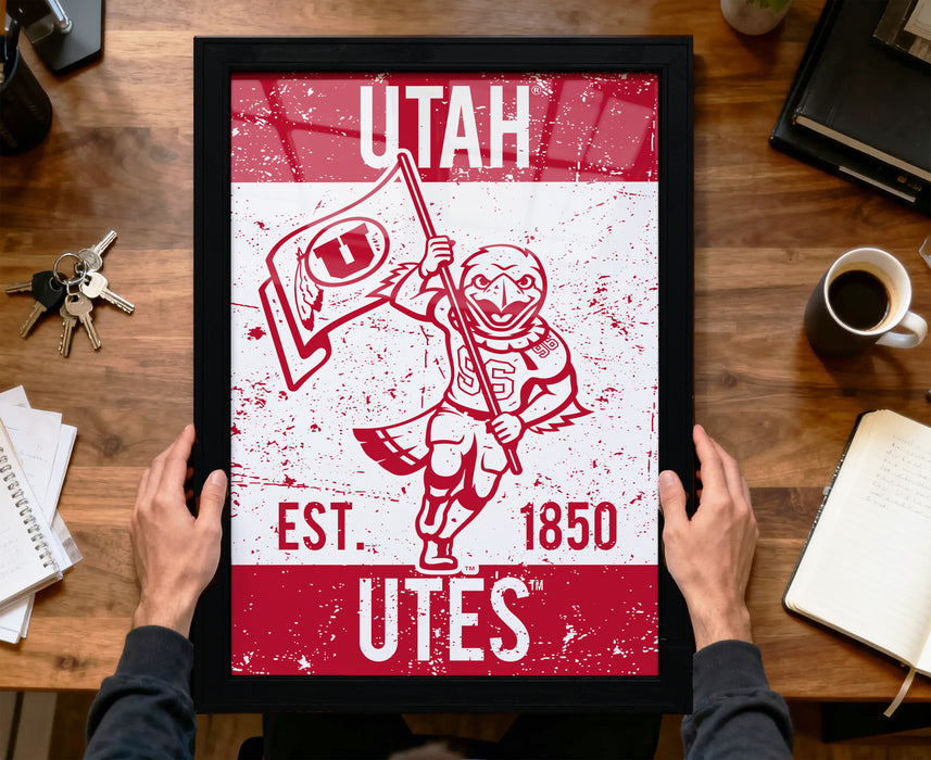 A framed poster of a red and white design featuring a bird character holding a flag, with text that reads "UTAH EST. 1850 Utes".