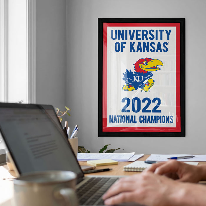 a framed poster of the University of Kansas football team, with a person's hands typing on a laptop in the foreground.