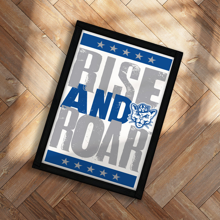 A framed poster with the text "RISE AND ROAR" and a logo, placed on a wooden floor.