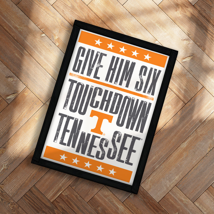 A framed poster with the text "GIVE HIM SIX TOUCHDOWN TENNESSEE" printed on it, placed on a wooden floor.