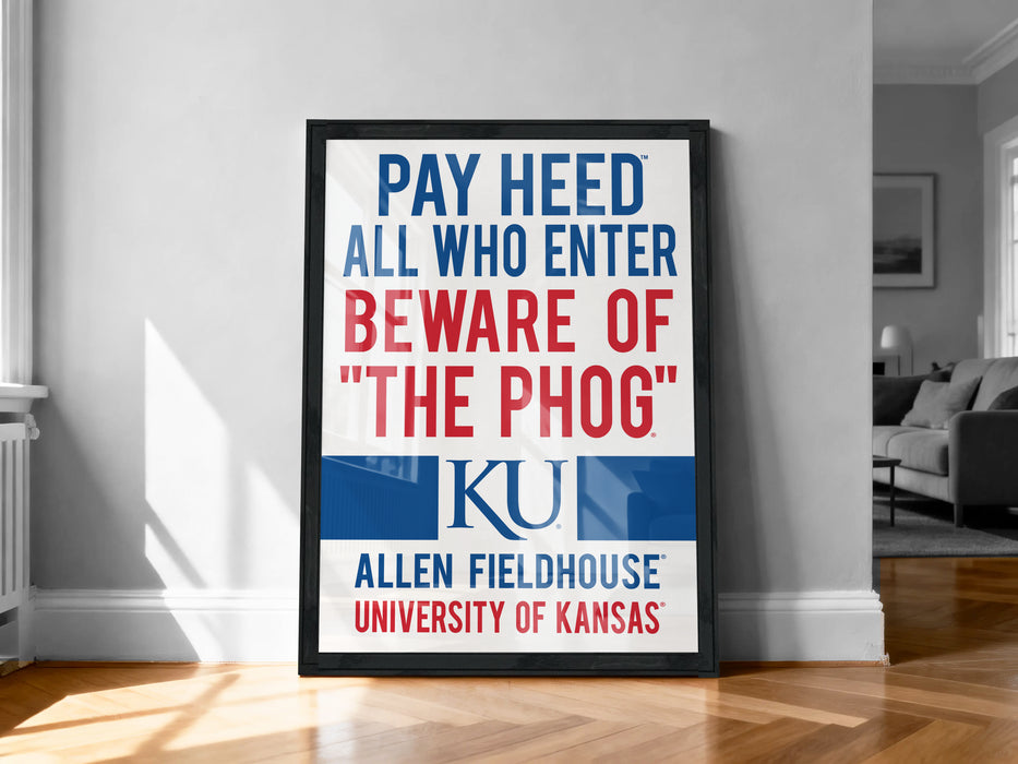 A framed poster with the text "PAY HEED ALL WHO ENTER BEWARE OF THE PHOG" and the university's logo, placed on a wooden floor against a white wall.