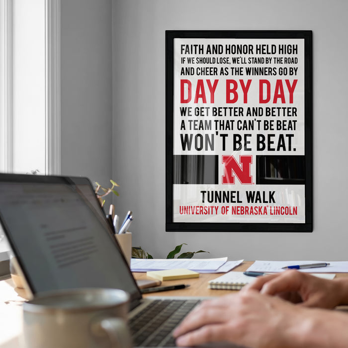 a poster with motivational text on the wall, a laptop on a desk, and a person's hands typing on the keyboard.