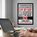 a poster with motivational text on the wall, a laptop on a desk, and a person's hands typing on the keyboard.